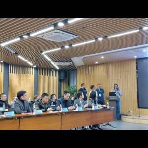 A conference room with attendees at a table listening to speakers, featuring modern decor and large screens.