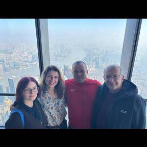 Four people pose together indoors with a city view in the background, featuring a river and tall buildings.
