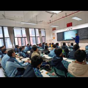 A classroom scene with students in blue uniforms attentively watching a teacher present on a screen.