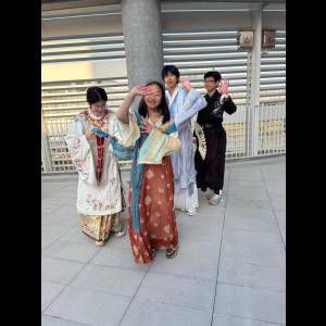 A group of four people in colorful traditional outfits smiles and poses playfully outdoors.