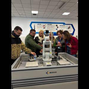 A group observes a robotic arm in a tech demonstration, engaging with automation equipment and learning.