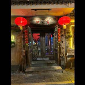 A wooden doorway with red lanterns, ornate details, and colorful lights creates a welcoming atmosphere at night.