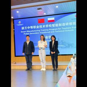 Three people stand in front of a banner, celebrating a training program for Polish vocational teachers in China.
