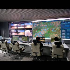 A high-tech control room with large screens displaying maps and live camera feeds, two operators monitor data.