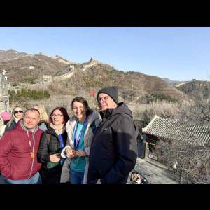 A group of four friends stands smiling at the Great Wall of China on a clear day.