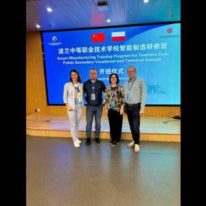 Group of four people at a ceremony for a Smart Manufacturing training program, with flags of China and Poland displayed.