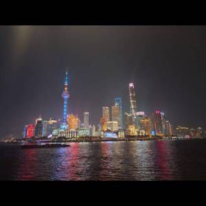 Brightly lit skyline of a modern city at night, showcasing tall buildings and vibrant reflections on the water.