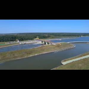 Aerial view of a river with a dam, surrounded by greenery and a clear blue sky.