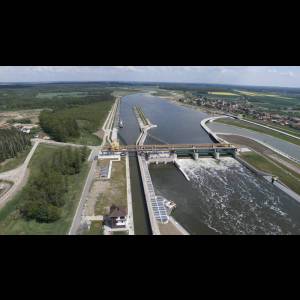 Aerial view of a dam and river system surrounded by greenery and farmland, with a boat navigating the water.
