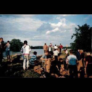 A group of people, including children, work together by a river, engaging in outdoor activities under a cloudy sky. Akcja układania worków w Rzeczycy/ Fot. arch. prywatne mieszkańców