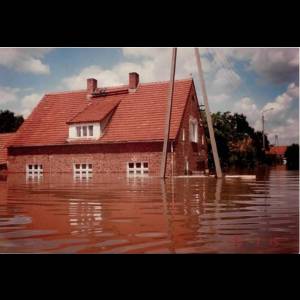 A partially submerged house surrounded by floodwaters, with power lines and a cloudy sky above. Rzeczyca/ Fot. J. Honc