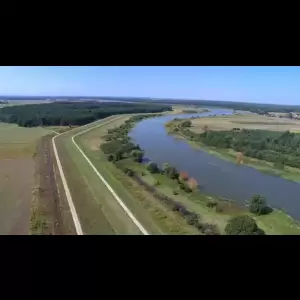 Aerial view of a winding river bordered by green fields and trees, under a clear blue sky.