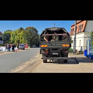 A military truck parked on a street, with soldiers inside and a group of people nearby.