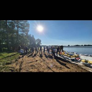 People working together on a sunny day by a river, setting up sandbags along the water's edge.