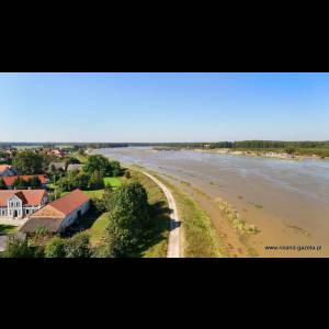 Aerial view of a calm river next to a village, featuring green fields, trees, and blue sky. Peaceful landscape scene.