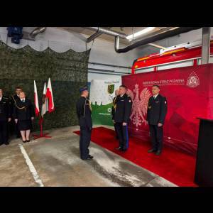 A formal ceremony featuring officials in uniforms with national flags and a podium, set in a garage-like environment.