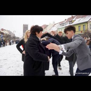 A group of people interacts in a snowy urban setting, with one person in a suit assisting another.