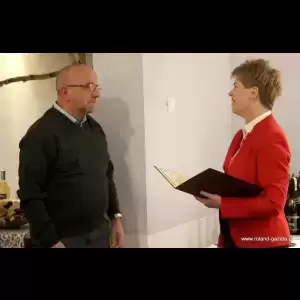 Klubu Honorowych Dawców Krwi „Kropelka Życia” A man in a sweater listens intently as a woman in a red blazer smiles while holding a document.