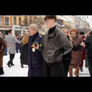 A snowy scene with people in winter clothes dancing, including a woman in uniform and a young man.