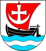 Herb gminy Malczyce: czarna łódź z czerwonym żaglem z białym krzyżem, płynąca po błękitno-białych falach na tarczy herbowej.