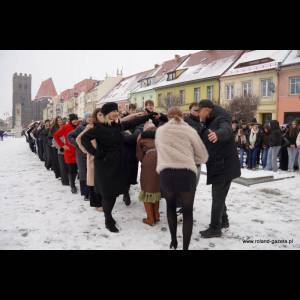 A group of people, dressed warmly, form a line in the snowy street, with colorful buildings in the background.