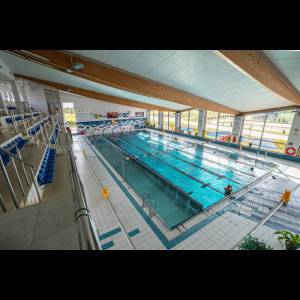 Indoor swimming pool with lanes, a spectator area, and natural light streaming through large windows.