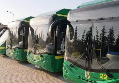 Rząd zielonych, nowoczesnych autobusów miejskich ustawionych na placu w Środzie Śląskiej; najbliższy oznaczony numerem 22, w tle drzewa i jasne światło dnia.