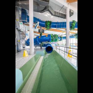 An indoor water park featuring blue slides, a green pool area, and safety signage.