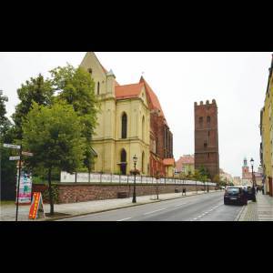 A street view featuring historic buildings, including a church and a tall brick tower, on a cloudy day.