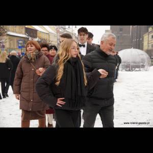 A group walks in the snow, with a girl and an older man holding hands at the front, enjoying the winter day.