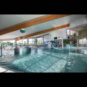 Indoor swimming pool with clear water, surrounded by large windows and wooden beams, creating a relaxing atmosphere.