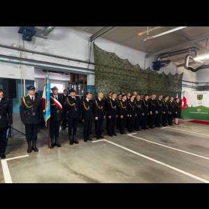 A formal event featuring a group of uniformed individuals standing in a row, with decorations and flags in the background.