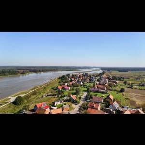 Aerial view of a serene landscape featuring a river, green fields, and a picturesque village with colorful houses.