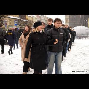 A crowd walks through snowy streets, with people dressed warmly and engaging in conversation.