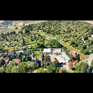 Aerial view of a green residential area with houses, gardens, and fields, showcasing natural beauty and development.