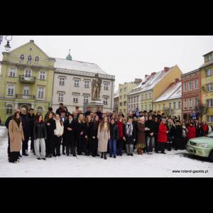 A large group of people poses for a photo in the snow near historic buildings and a statue.