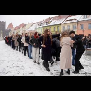 A line of people dressed in various outfits stands in the snow, posing in a colorful town square.