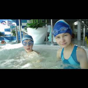 Two girls in swimwear and goggles enjoy a bubbly pool, smiling amidst a vibrant water park setting.