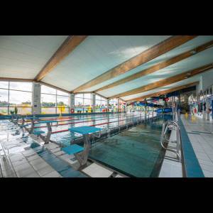 Bright indoor swimming pool with diving boards, wooden beams, and play area visible in the background.