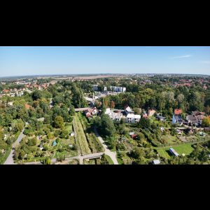 Aerial view of a lush landscape with houses, trees, and gardens under a clear blue sky.