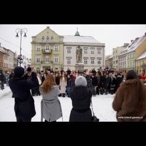 A large group of people gathers for a photo in a snowy town square with historical buildings and a statue.