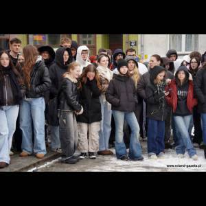 A large group of mostly young people stand together outside, bundled in winter clothing, amidst a snowy scene.