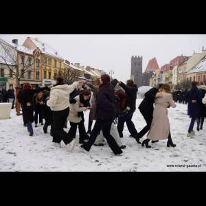 People bundled up in winter clothes gather in a snowy square, engaged in a lively group activity.