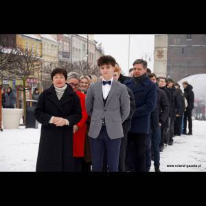 A group of people in winter clothing stands in a line in a snowy outdoor setting, smiling and chatting.