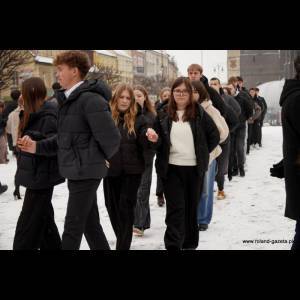 A line of young people in winter clothing walking on snow-covered pavement in a city street.